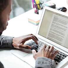 Cropped photo of serious young man sitting in office coworking. Looking aside using laptop computer. Focus on computer.